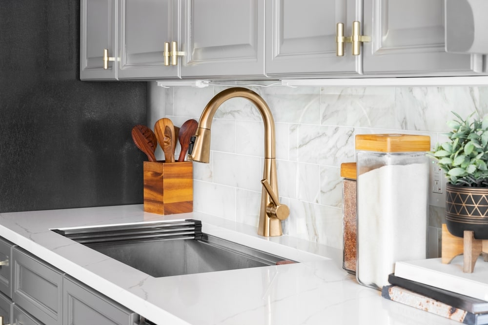 kitchen cabinets painted gray with brass hardware and a marble subway tile background